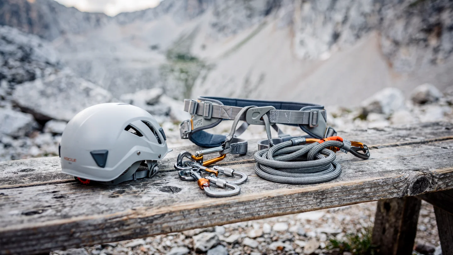 An illustrative climbing helmet, harness and lanyard on a wooden bench